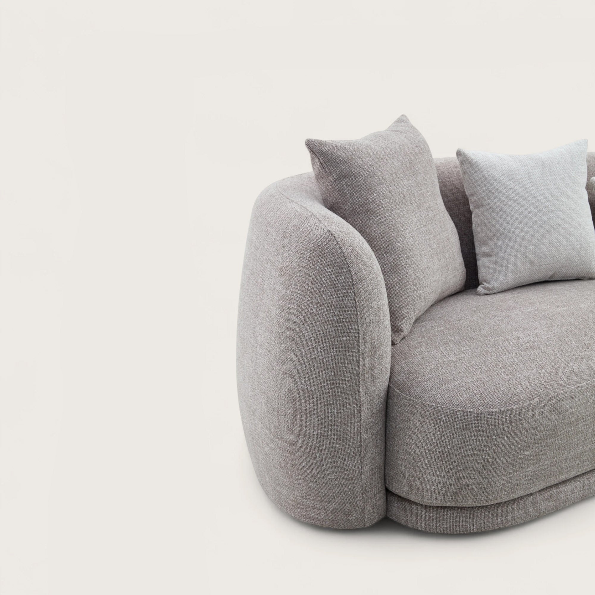 Divano dal design moderno e elegante in tessuto tortora con forma curva e asimmetrica, divano imbottito e braccioli avvolgente e confortevoli con angoli arrotondati.