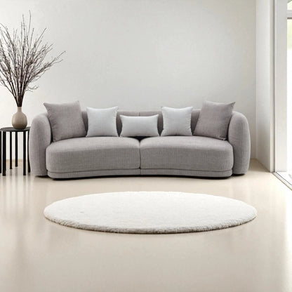 Divano Ethan 3 posti in tessuto tortora con forma curva e asimmetrica, seduta ergonomica da 60 a 68 cm, imbottitura avvolgente e design moderno ed elegante per soggiorno raffinato.