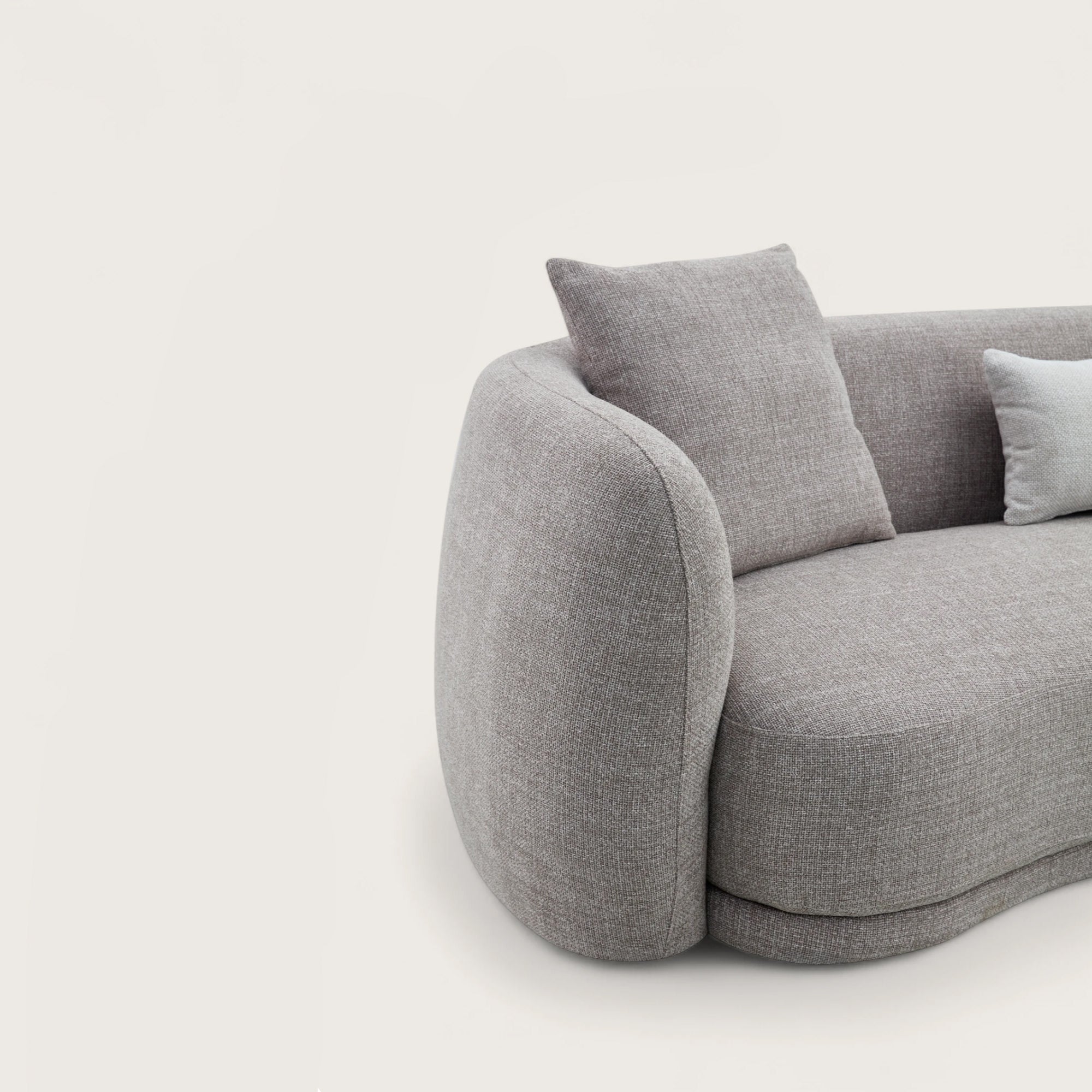 Divano dal design moderno e elegante in tessuto tortora con forma curva e asimmetrica, divano imbottito, braccioli avvolgente e confortevoli con angoli arrotondati.